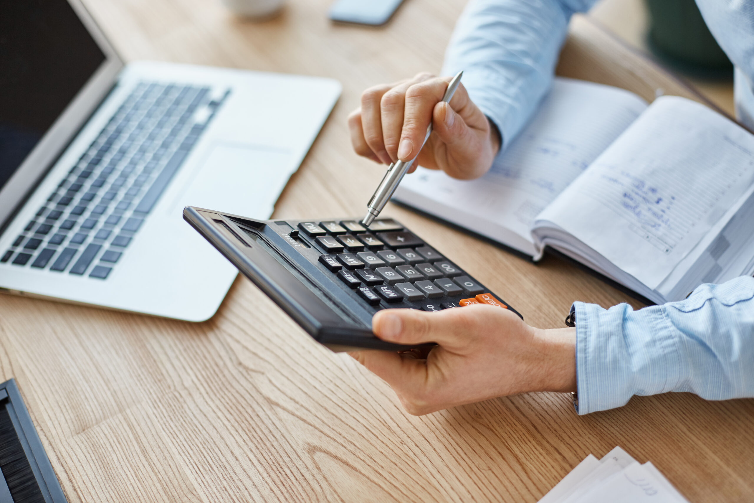 Pessoa segurando uma calculadora em cima de uma mesa de trabalho