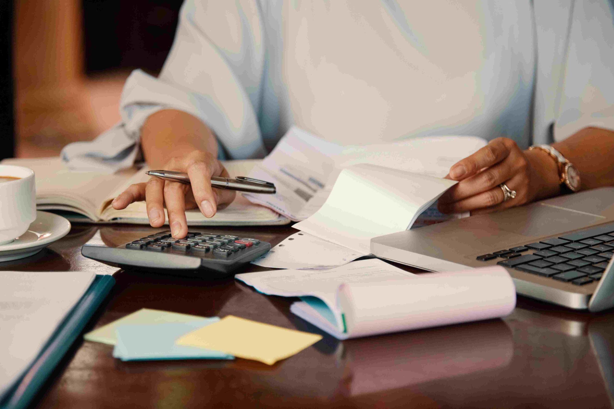 Mulher fazendo contas em uma calculadora com papéis em volta