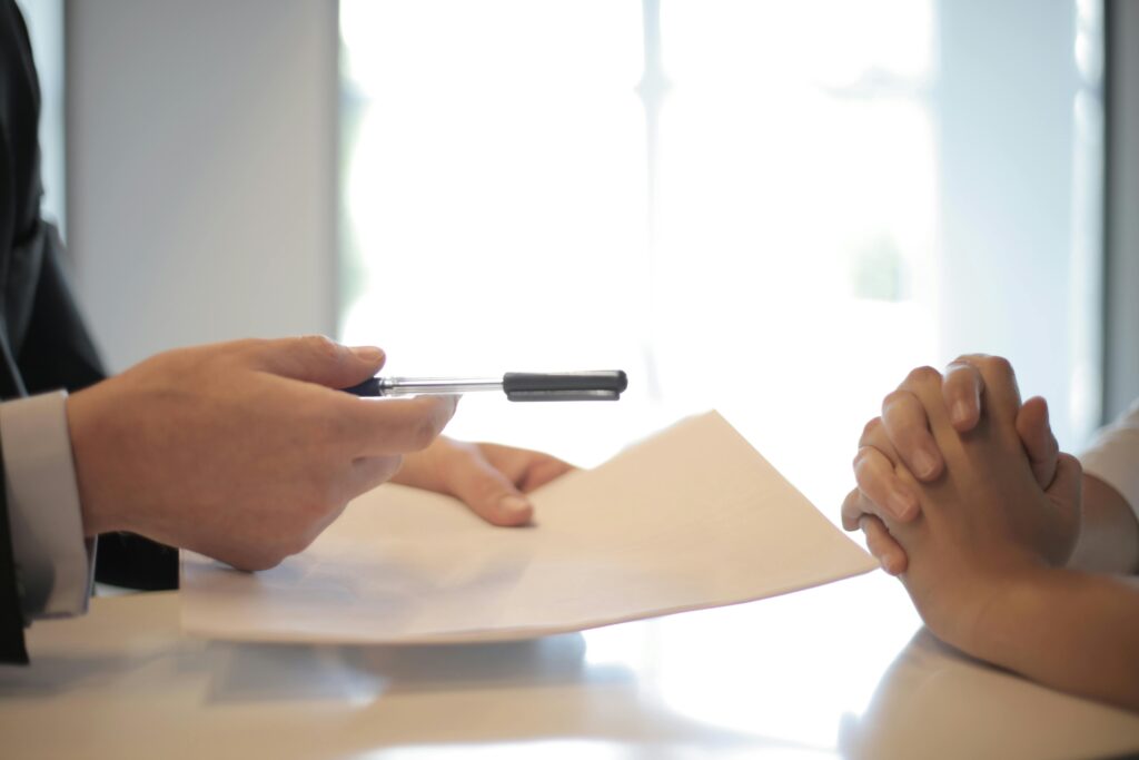 Uma pessoa entregando um papel e uma caneta para outra pessoa assinar o registro INPI 