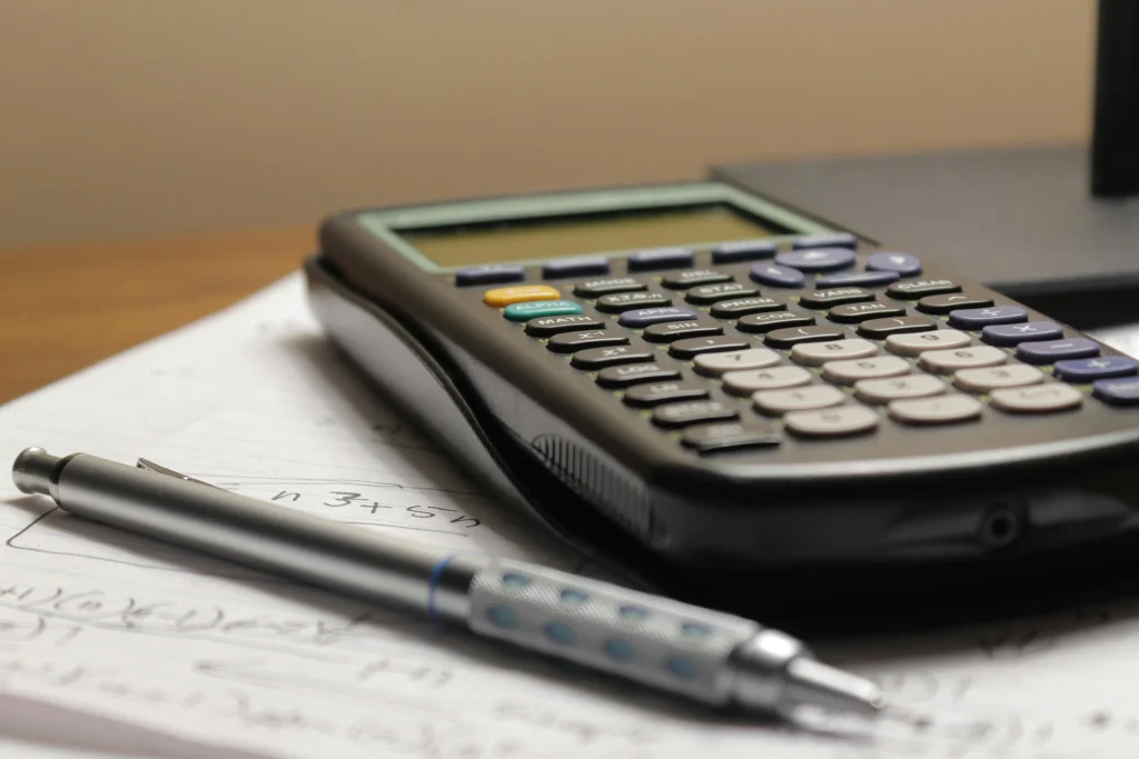 uma mesa com uma calculadora um papel e uma caneta para calcular custos